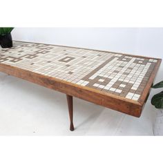 a wooden table with white and brown tiles on it next to a potted plant