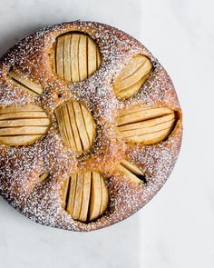 an apple pie is topped with powdered sugar and sliced almonds on a white surface