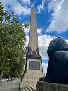 the obelisk is next to a statue in front of some trees and people