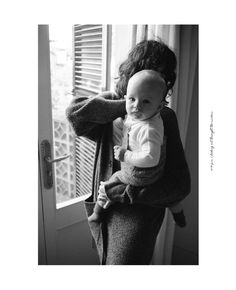 a woman holding a baby up to her face in front of a window with shutters