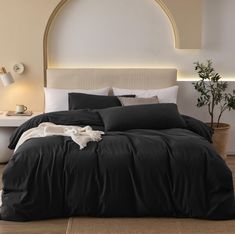 a bed with black linens and pillows in a white room next to a potted plant