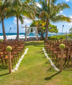 an outdoor ceremony set up with wooden chairs and flower arrangements on the grass near the ocean