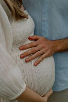 a pregnant woman is holding her husband's belly while he holds his hand on the stomach