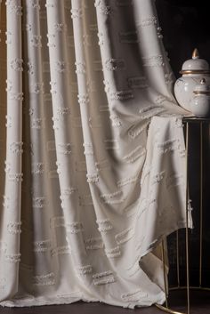 a white curtain with ruffles on it next to a gold stand and lamp