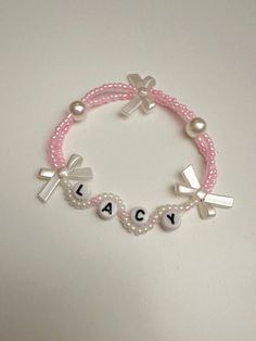 a pink beaded bracelet with two crosses and name charms on it, sitting on a white surface