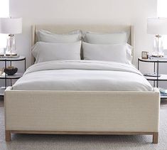 a bed with white linens and pillows in a large room next to two nightstands