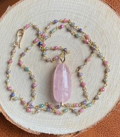 "This soft pastel colored multi Sapphire necklace featuring a stunning centerpiece, a large peachy pink Morganite pendant, captures the essence of the season, radiating femininity. The large, smooth polished natural pink Morganite pendant measures 2.2 x 1.1 cm. This alluring gemstone is suspended from a 19.5\" (50 cm) long multicolor Sapphire rosary chain, fastened by a hand forged 14k gold filled hook clasp. The sparkly multi Sapphire rosary chain boasts a luxurious 22k gold vermeil finish. The Feminine Oval Pink Jewelry, Pink Oval Feminine Jewelry, Feminine Pink Oval Jewelry, Pink Spiritual Pendant Crystal Necklace, Spiritual Pink Pendant Crystal Necklace, Pink Round Gemstone Beads Necklace, Pink Gemstone Bead Necklaces, Pink Gemstone Beads Crystal Necklace Gift, Pink Pendant Crystal Necklace With Natural Stones