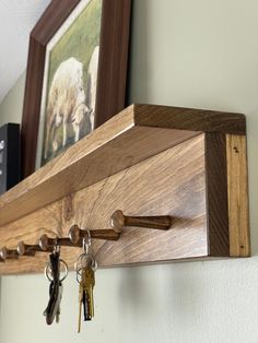 a wooden key rack with keys hanging from it's sides and two framed pictures on the wall