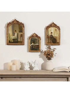 three paintings hang on the wall above a table with candles and flowers in vases