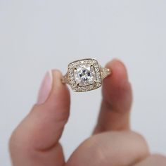 a woman's hand holding an engagement ring with a square shaped diamond in the center