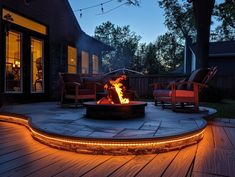 an outdoor fire pit lit up at night on a deck with chairs and lights around it