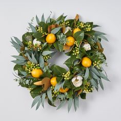 a wreath with oranges and green leaves on a white background, surrounded by greenery