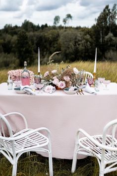 the table is set with pink flowers and candles for an outdoor wedding reception in tall grass