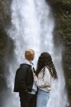 a man and woman standing in front of a waterfall