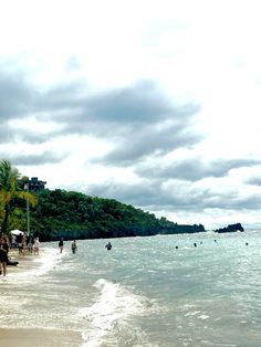 people are walking on the beach near the water and palm trees in the foreground