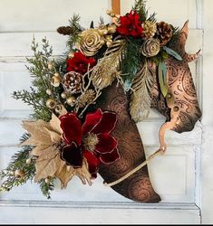 a horse head decorated with flowers and pine cones on a door hanger in front of a white wall