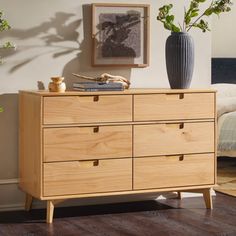 a wooden dresser with two vases on top of it and a bed in the background