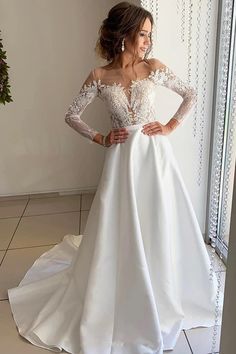 a woman in a white wedding dress standing next to a window with her hands on her hips