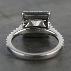 a ring with a princess cut diamond in the center on a gray surface, set against a black background