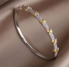 Elevate your style with our stunning Two-Tone Crystal Bangle Bracelet, an exquisite piece of jewelry that perfectly blends elegance and sophistication. This bracelet features a unique design with alternating bands of silver and gold, adorned with sparkling crystal accents that catch the light beautifully. The distinctive gold X details add a touch of modern charm, making this bangle a versatile accessory for any occasion. Crafted with high-quality materials, this bangle bracelet is both durable Unique Bracelets Gold, Modern Gold Jewelry Unique Designs, Silver Bangle Bracelets Unique, High Jewelry Bracelet, Modern Bangle, Necklace Chain Types, Modern Gold Jewelry, Jewelry Illustration, The Bangles