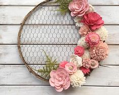 a wreath made out of flowers on top of a white wooden table next to a chicken wire fence