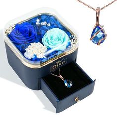 an open jewelry box with blue roses and pearls in it next to a necklace on a chain