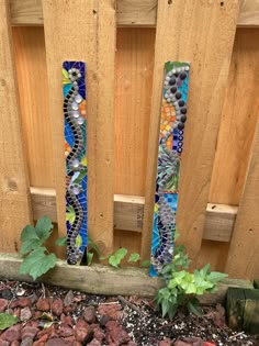 two decorative pieces of glass sitting on top of a gravel ground next to a wooden fence