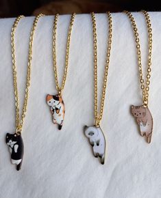 four different necklaces with cats on them sitting on top of a white cloth covered surface