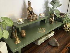 a green table with candles and statues on it next to a potted houseplant