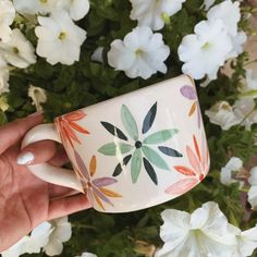 a hand holding a coffee cup with flowers in the background