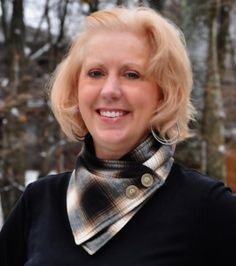 a woman with blonde hair wearing a black shirt and plaid scarf smiling at the camera