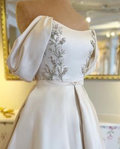 the back of a wedding dress on display in front of a gold framed mirror,