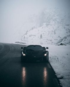 a black sports car driving down a snow covered road in front of a snowy mountain