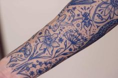 a person's arm with tattoos on it and blue flowers in the middle of their arm