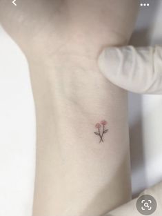 a small pink flower tattoo on the left side of the ankle, with an arrow at the center