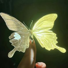 a yellow butterfly is being held by someone's hand in front of a black background