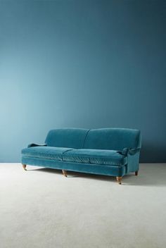 a blue couch sitting on top of a white floor next to a blue wall and lamp