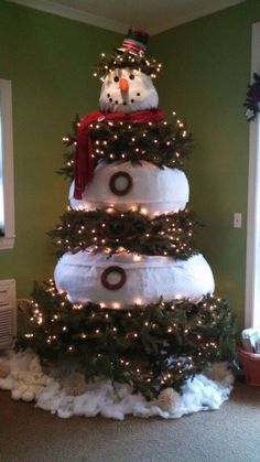 a snowman is sitting on top of a christmas tree made out of pillows and lights