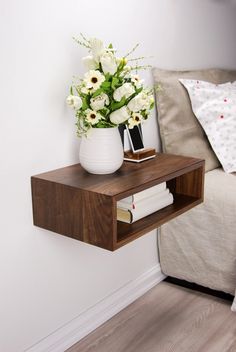 a vase with flowers on top of a wooden shelf next to a bed and pillows