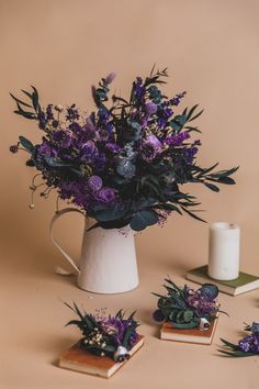 purple flowers are in a white pitcher next to small coasters with candles on them