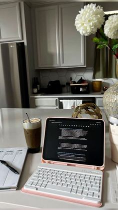 an open laptop computer sitting on top of a white desk next to a vase with flowers