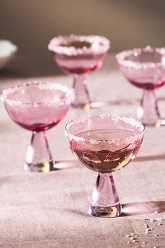 several pink wine goblets are lined up on a table with white speckles