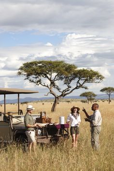 two people are standing in the tall grass near an open vehicle with food on it