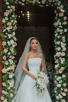 a woman in a wedding dress standing next to a flower arch