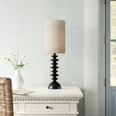 a lamp sitting on top of a white table next to a vase with flowers in it