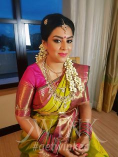 a woman in a yellow and green sari sitting on a wooden floor next to a window