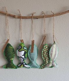 four fish shaped ornaments hang from a branch on the wall in front of a white wall