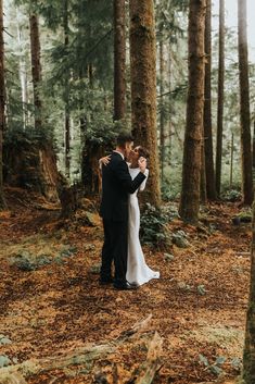 a bride and groom standing in the middle of a wooded area with their arms around each other