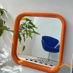 an orange framed mirror sitting on top of a white wall next to a blue chair