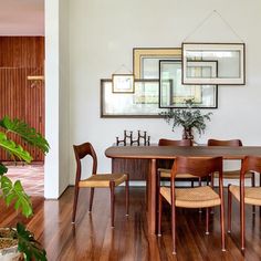 a dining room table with chairs and pictures on the wall above it, along with potted plants